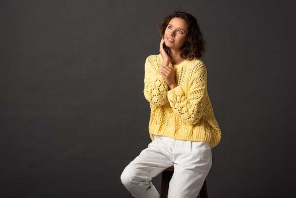 dreamy curly woman in yellow knitted sweater looking away on black background - Fotoğraf, Görsel