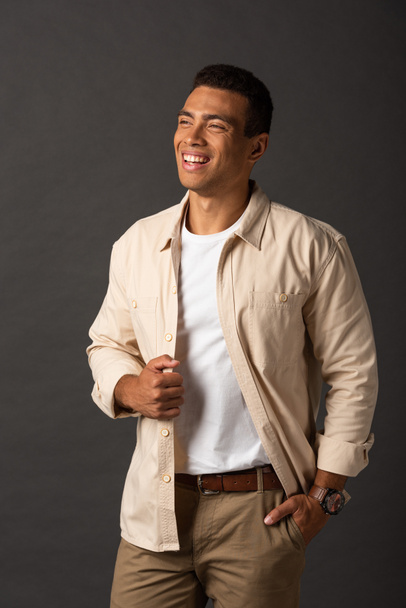 heureux beau mixte homme en chemise beige avec la main dans la poche sur fond noir
 - Photo, image