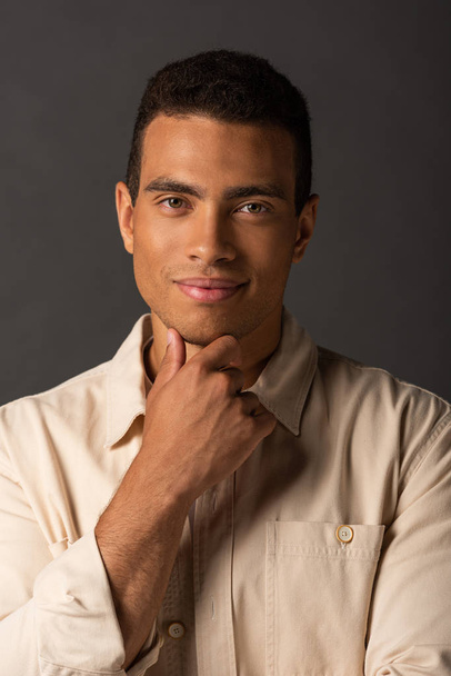 portrait of smiling handsome mixed race man in beige shirt on black background - Фото, изображение