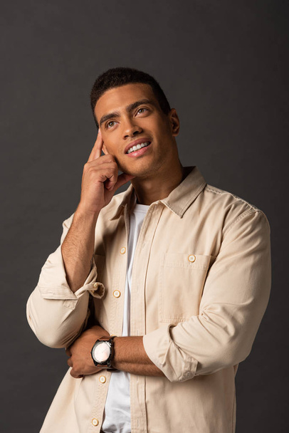 dreamy handsome mixed race man in beige shirt on black background - Фото, изображение