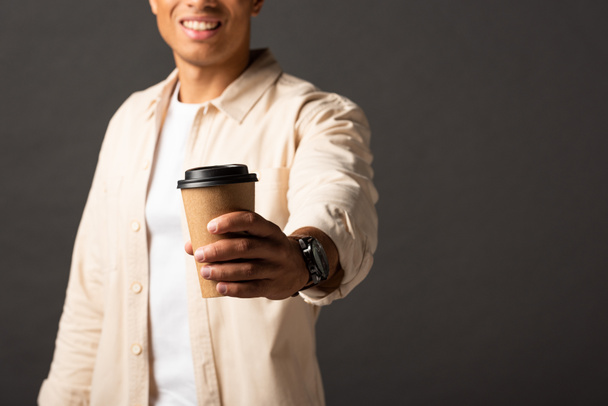 cropped view of mixed race man in beige shirt holding coffee to go on black background - Photo, Image