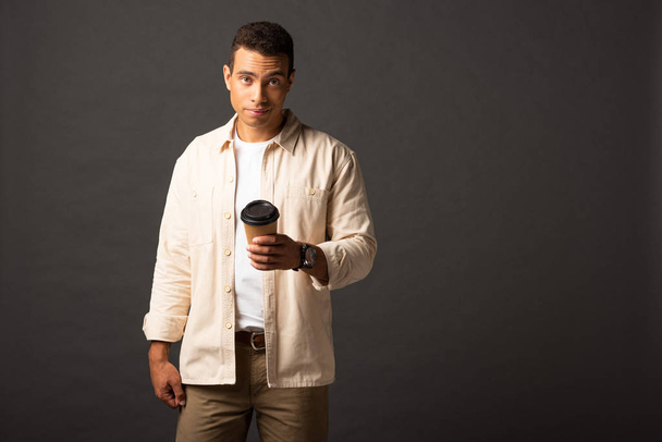 pohledný smíšený člověk v béžové košili držící kávu na černém pozadí - Fotografie, Obrázek