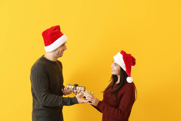 Happy young man and woman giving each other Christmas presents against color background - Foto, immagini