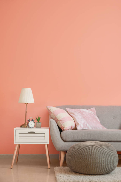 Acogedor sofá con puf y mesa cerca de la pared de color en la habitación
 - Foto, Imagen