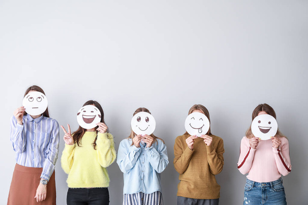 Группа женщин, покрывающих свои лица нарисованными смайликами на светлом фоне
 - Фото, изображение