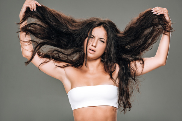 brunette beautiful woman holding wavy hair isolated on grey - 写真・画像