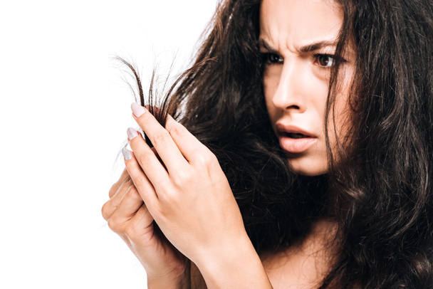 gestresste brünette Frau sieht beschädigtes trockenes Haar isoliert auf weißem Grund - Foto, Bild
