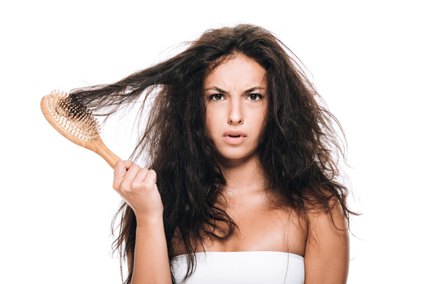 napjatá brunetka držící vlnité vlasy v hřebenu izolované na bílém - Fotografie, Obrázek