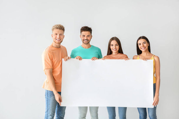 Gruppe junger Leute in stylischer Freizeitkleidung und mit leerem Poster auf hellem Hintergrund - Foto, Bild