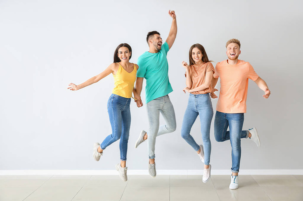 Gruppe springender junger Leute in stylischer Freizeitkleidung nahe Lichtwand - Foto, Bild