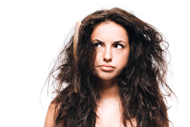 verwirrte brünette Frau mit Haarbürste im widerspenstigen lockigen Haar isoliert auf weiß - Foto, Bild