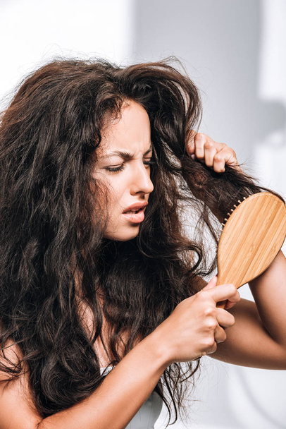 mulher morena confusa styling cabelo encaracolado indisciplinado com escova de cabelo
 - Foto, Imagem