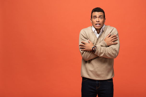 confused mixed race man in beige sweater feeling cold isolated on orange - Фото, зображення