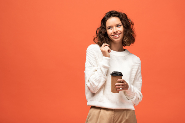 smiling shy woman holding coffee to go isolated on orange - Photo, Image