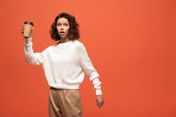 shocked woman holding coffee to go isolated on orange - Fotó, kép
