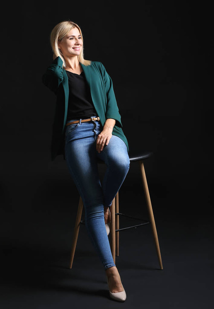 Beautiful stylish businesswoman sitting on chair against dark background - Fotoğraf, Görsel