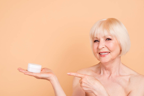 Close up photo beautiful amazing mature she her aged model lady recommend new procedures hold indicate arm hand cream aesthetic pretty ideal appearance wear nothing isolated pastel beige background - 写真・画像