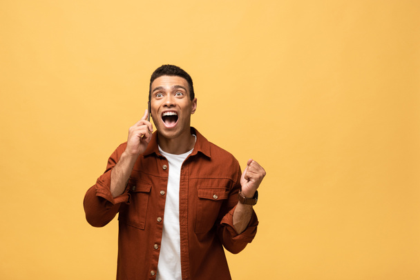 happy mixed race man talking on smartphone and showing yes gesture isolated on yellow - Photo, Image