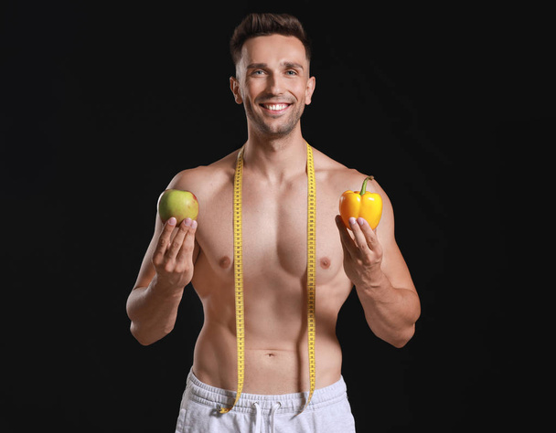 Handsome muscular man with measuring tape and food on dark background. Weight loss concept - Foto, Bild