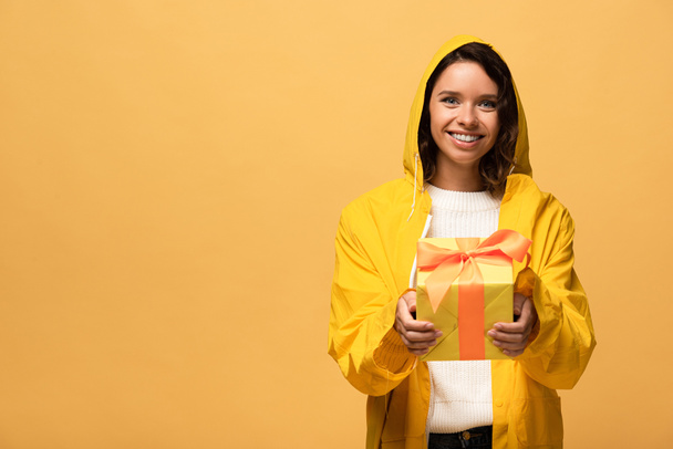 onnellinen kihara nainen keltainen sadetakki tilalla lahjapaketti eristetty keltainen
 - Valokuva, kuva