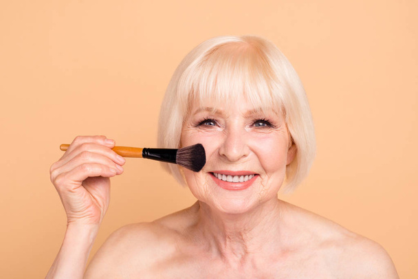 Close-up portrait of her she nice-looking attractive lovely groomed cheerful gray-haired lady applying powder instant effect facial sculpturing isolated over beige background - Foto, Bild