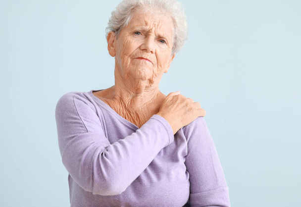 Vanhempi nainen, joka kärsii hartiakivusta valoisaa taustaa vasten
 - Valokuva, kuva