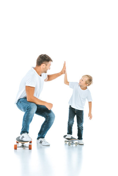 happy father giving high five to cheerful son riding penny board on white  - Fotó, kép