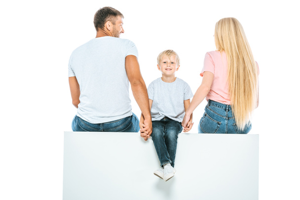 parents sitting on cube and holding hands with cheerful son isolated on white  - Foto, Bild
