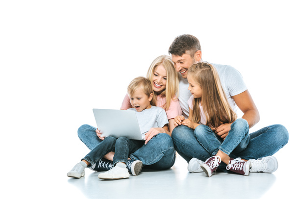 vrolijke ouders kijken naar laptop in de buurt van kinderen op wit  - Foto, afbeelding