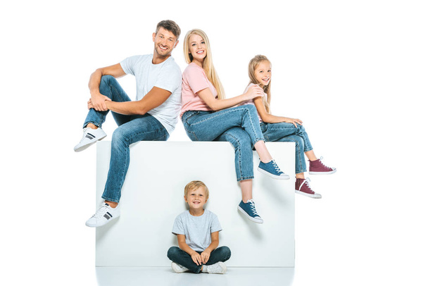 happy family sitting on cube and looking at camera on white - Zdjęcie, obraz