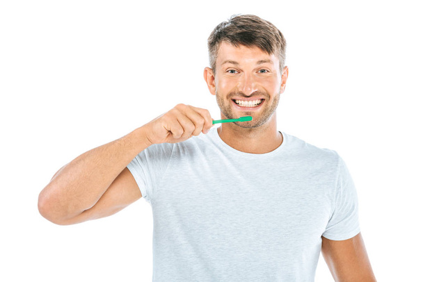 glücklicher Mann mit Zahnbürste, während er isoliert auf weißem Grund lächelt  - Foto, Bild