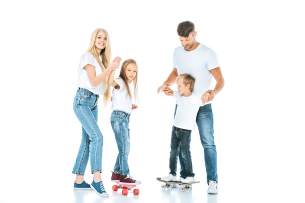genitori felici vicino tenere le mani dei bambini che cavalcano penny board su bianco
  - Foto, immagini