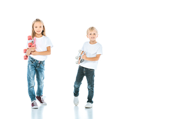 niños felices sonriendo mientras miran a la cámara y sostienen penny boards en blanco
  - Foto, Imagen