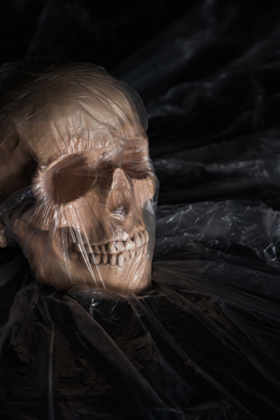 spooky human skull in cellophane on black background, Halloween decoration - Photo, Image