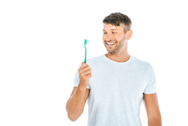 hombre alegre mirando cepillo de dientes mientras sonríe aislado en blanco
  - Foto, Imagen