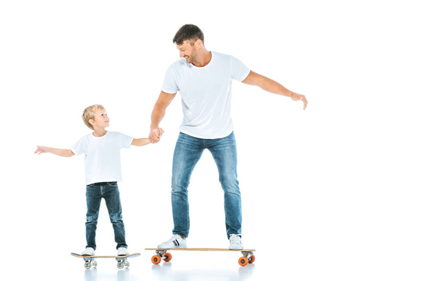 happy father and son holding hands while riding penny boards on white  - Foto, Imagem