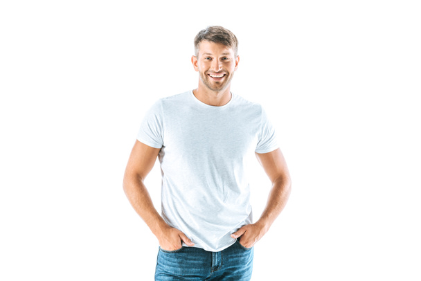 cheerful and handsome man standing with hands in pockets isolated on white  - Foto, Imagem