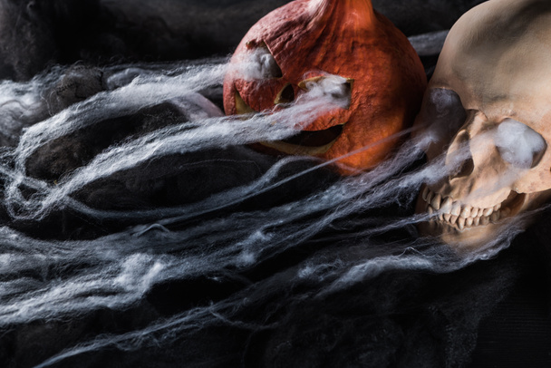 spooky human skull and carved Halloween pumpkin on black background - Foto, Imagen