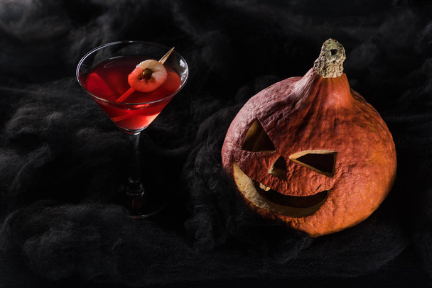 rood ingericht Halloween cocktail in de buurt van Spooky pompoen in zwarte wolken - Foto, afbeelding