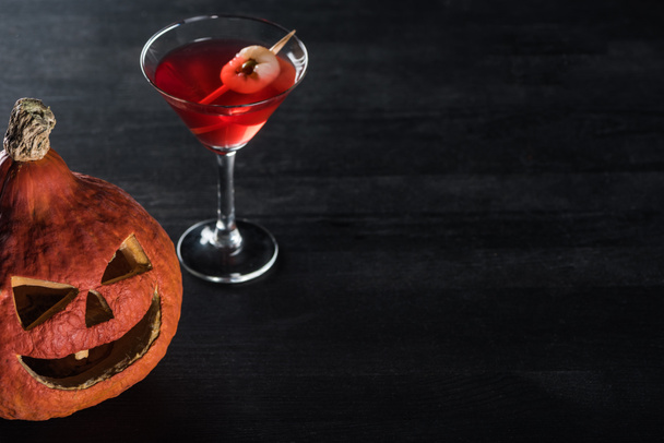 Gruseliger Halloween-Kürbis und roter Cocktail auf schwarzem Hintergrund - Foto, Bild
