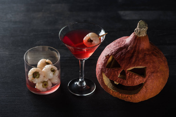 Gruselig geschnitzter Halloween-Kürbis und roter Cocktail auf schwarzem Hintergrund - Foto, Bild