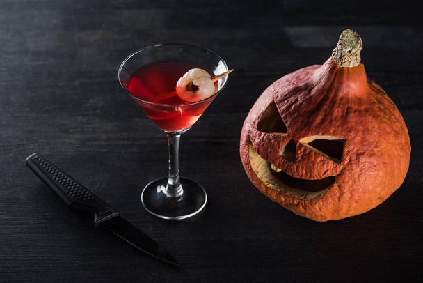 Spooky Halloween pompoen, mes en rode cocktail op zwarte achtergrond - Foto, afbeelding
