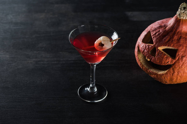 carved Halloween pumpkin and red cocktail on black background - Фото, изображение