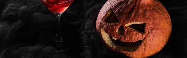 panoramic shot of red decorated Halloween cocktail near spooky pumpkin in black clouds - Foto, Imagem