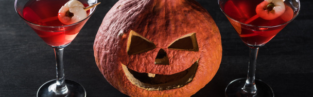 panoramic shot of spooky Halloween pumpkin and red cocktails on black background - Фото, зображення
