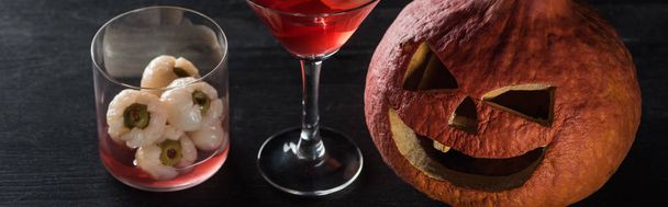 panoramic shot of spooky Halloween pumpkin and red cocktail on black background - Photo, Image