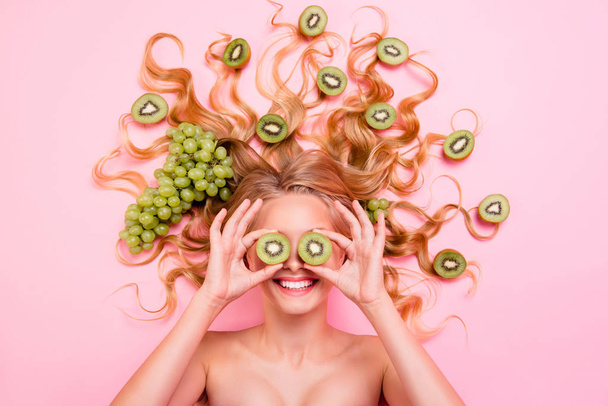 Close up top above high angle view photo beautiful she her lady lying down grape fruits in long curly wavy hair cover eyes kiwi slice specs healthy lifestyle eating feeding isolated pink background - Photo, Image
