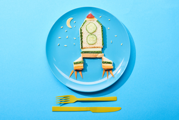 вид зверху на тарілку з ракетою з їжі для дитячого сніданку біля столових приборів на синьому фоні
 - Фото, зображення