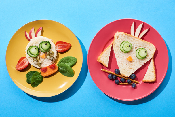 верхний вид тарелок с модной коровой и птицей, изготовленных из продуктов питания для детей завтрак на синем фоне
 - Фото, изображение