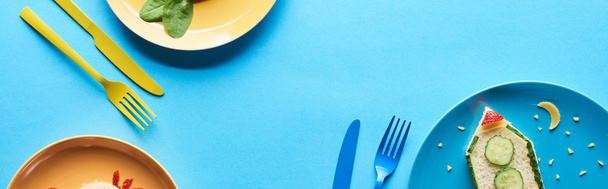top view of plates with fancy childrens breakfast near cutlery on blue background, panoramic shot - Photo, Image
